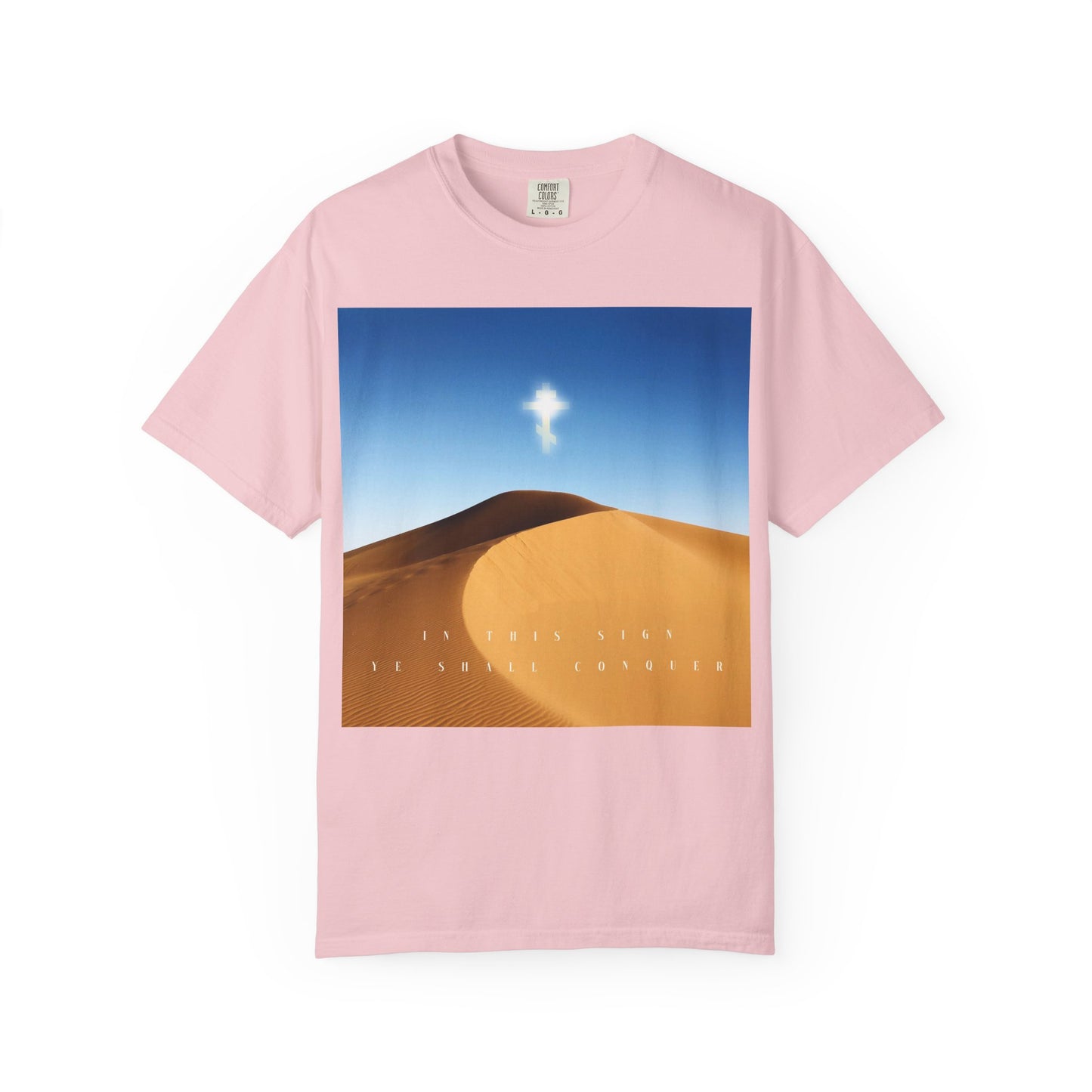 Blossom-colored heavyweight cotton unisex tee featuring a desert sun scene, blue sky, a glowing cross symbolizing the Elevation of the Cross, and the text: IN THIS SIGN YOU SHALL CONQUER.