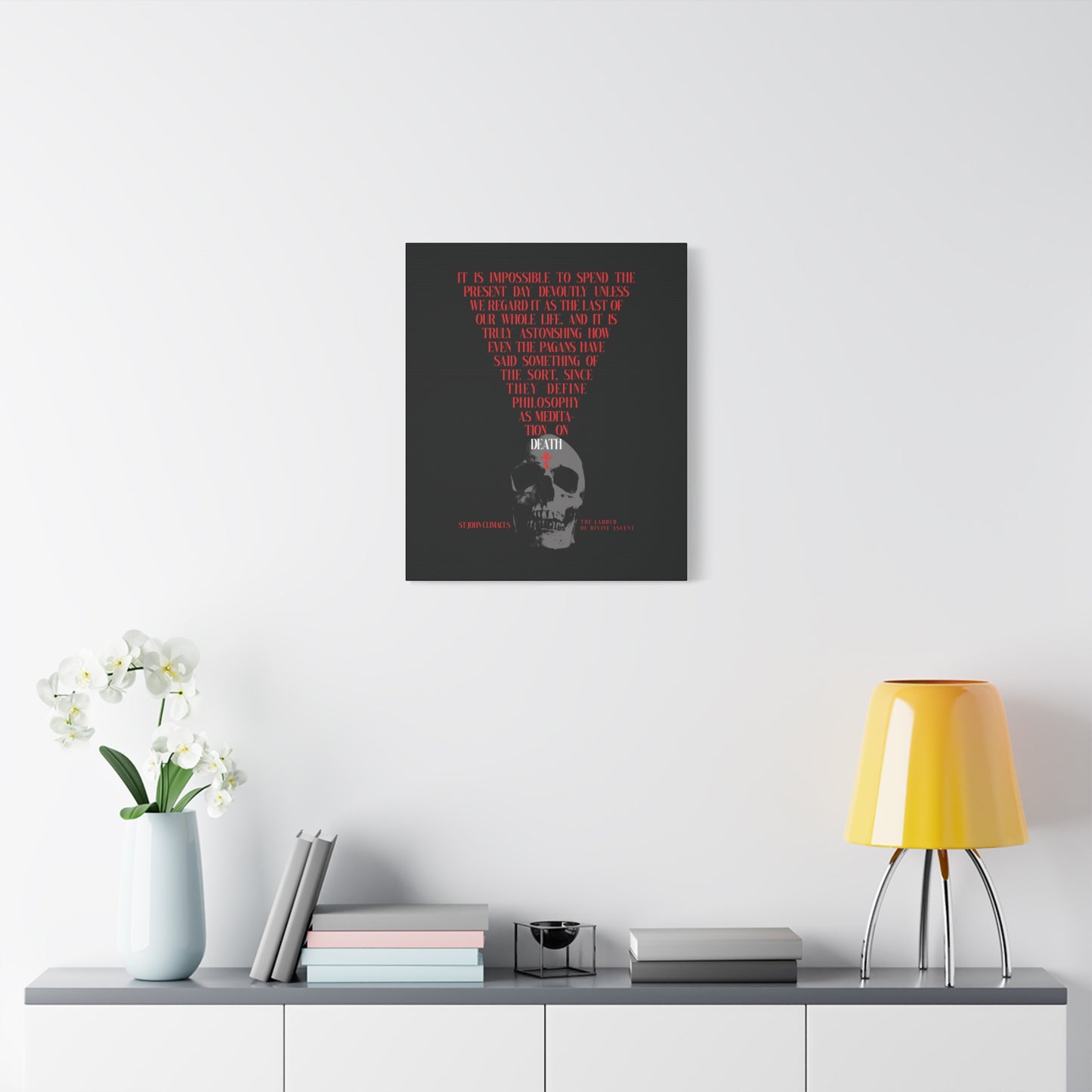 Minimalist room featuring “The Present Day As the Last Day of Our Life” Orthodox canvas art with skull and red cross, console table, yellow lamp, and flowers—offering a subtle memento mori inspired by St John Climacus.