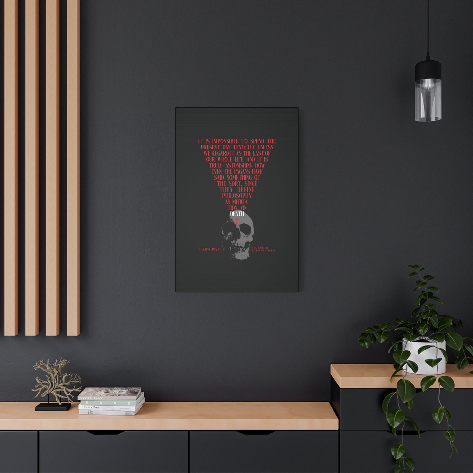 A dark room features "The Present Day As the Last Day of Our Life | St John Climacus | Skull with Red Orthodox Cross" Orthodox canvas wall art above a black cabinet decorated with books, a bonsai, and a plant.