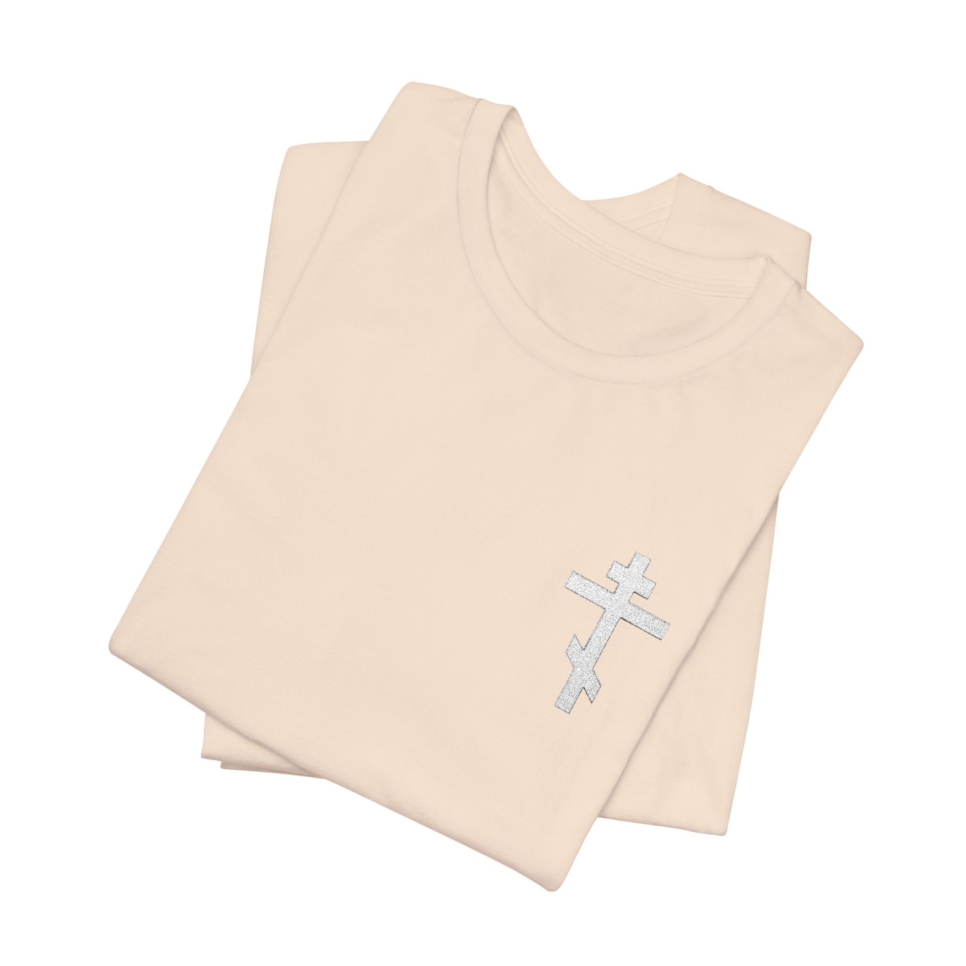 Two folded May I Never Boast Except in the Cross (Gal 6:14) Christian Cotton Unisex T-Shirts in beige, with small embroidered white Orthodox crosses on the chest, made from soft Airlume combed cotton jersey, shown on a white background.