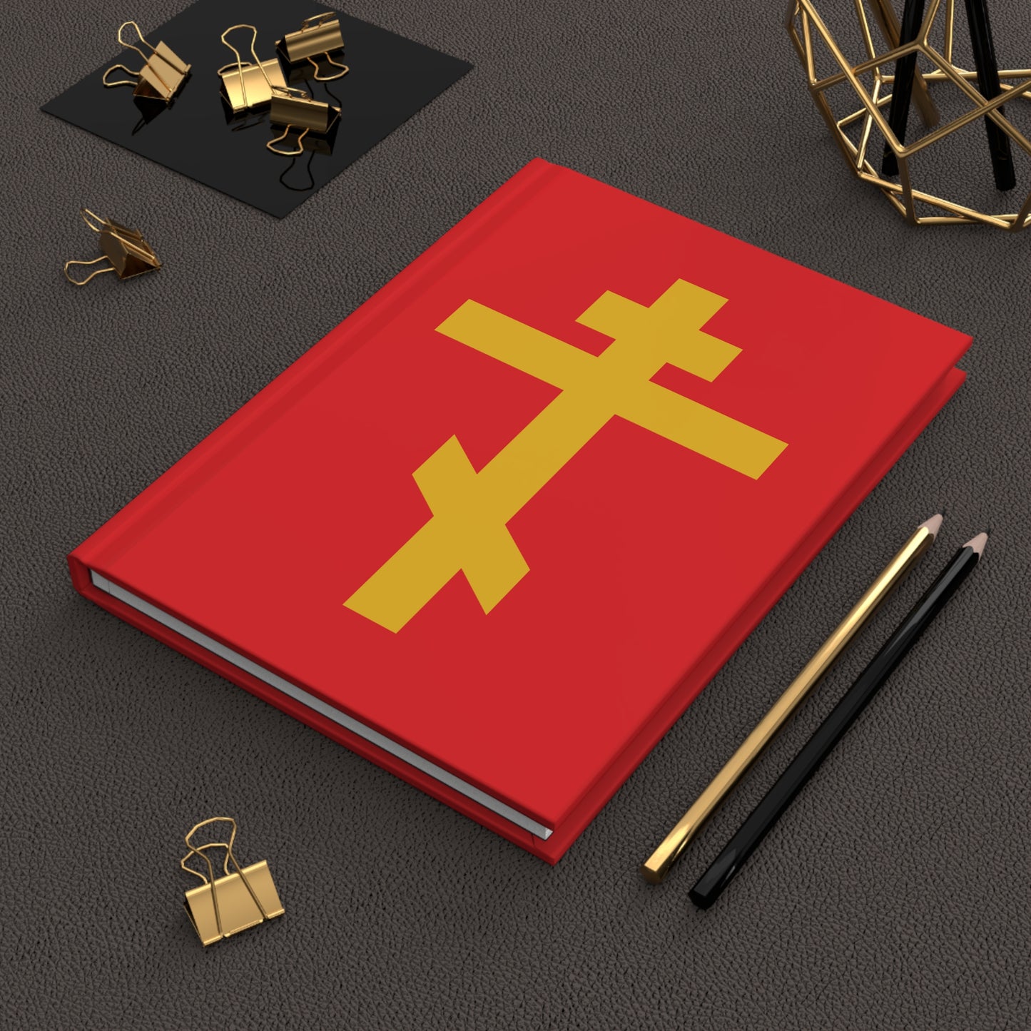 A "Yellow Orthodox Cross Red Background" Orthodox Hardcover Journal—a precious, life-giving weapon of unseen warfare and scourge of demons—rests near pencils and gold binder clips on a desk.