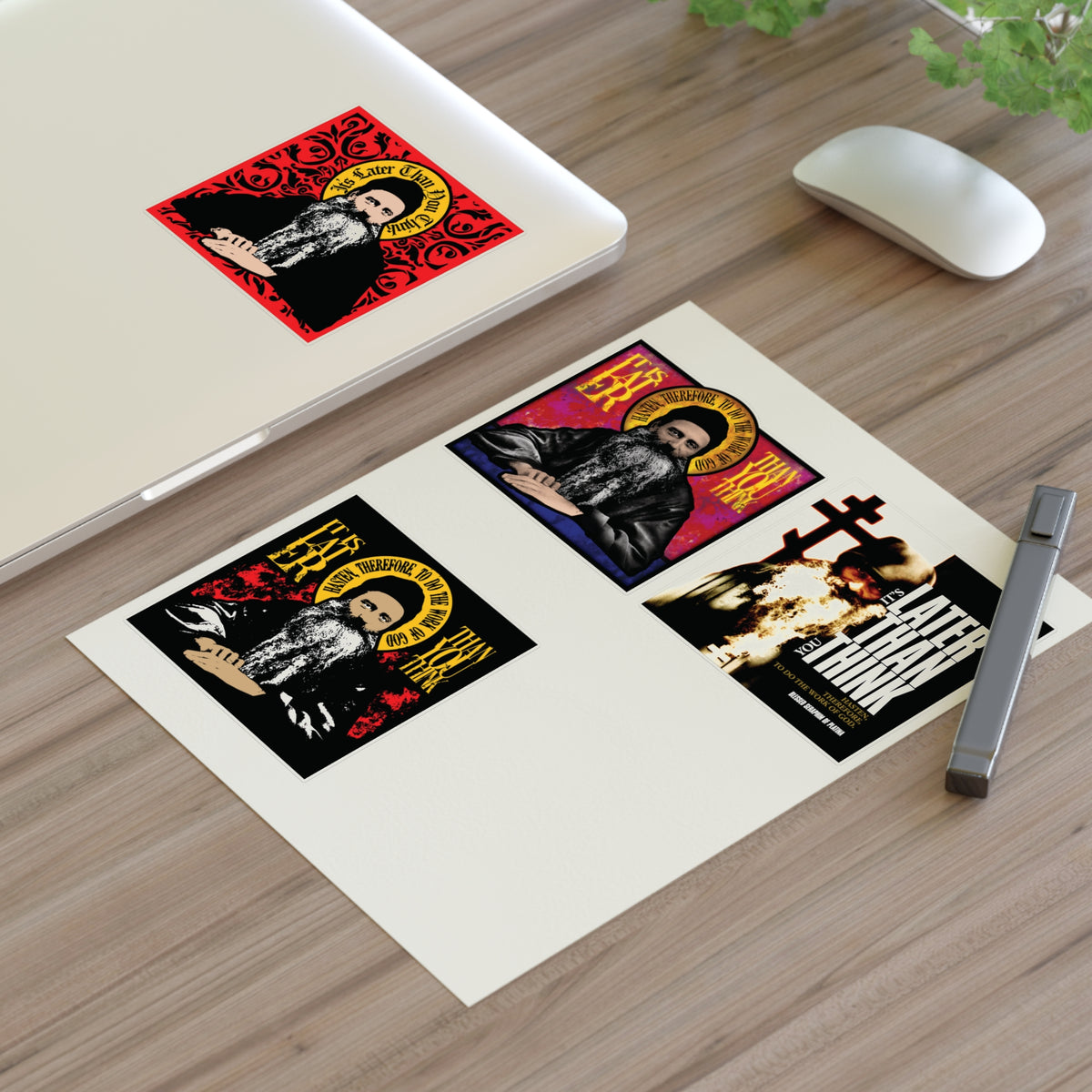 Laptop with red sticker, Fr Seraphim Rose Four Sticker Sheet No. 1 on paper, mouse, pen, and plant on desk.