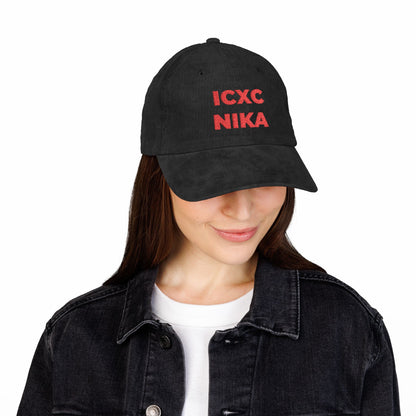 Woman wearing a red ICXC NIKA Text Christogram cap, an embroidered cotton corduroy hat symbolizing "Jesus Christ Conquers," paired with a black denim jacket and white shirt.