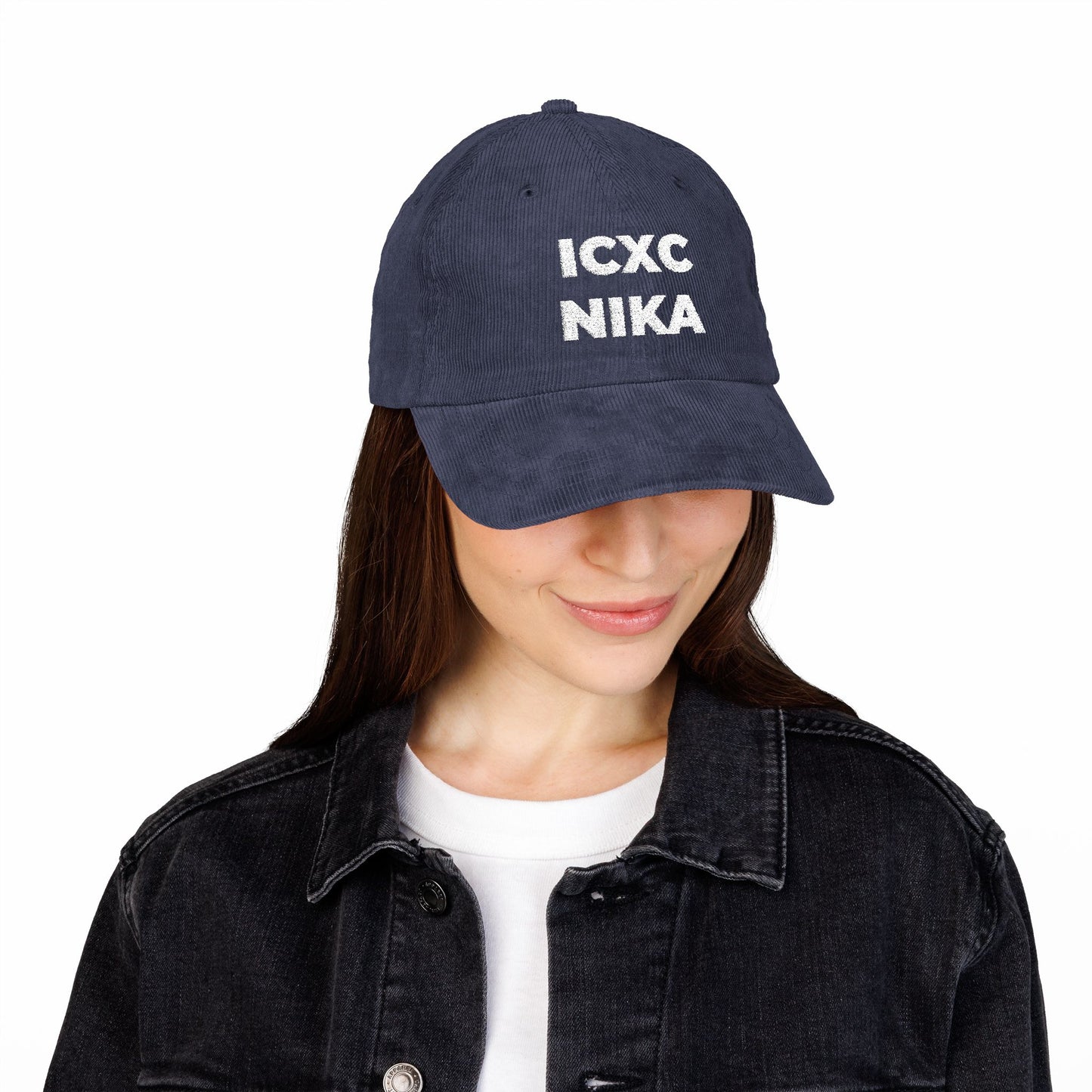 Woman wearing a White ICXC NIKA Text Christogram cap—an embroidered cotton corduroy hat with the Orthodox Christian symbol meaning "Jesus Christ Conquers"—paired with a black denim jacket and white shirt.
