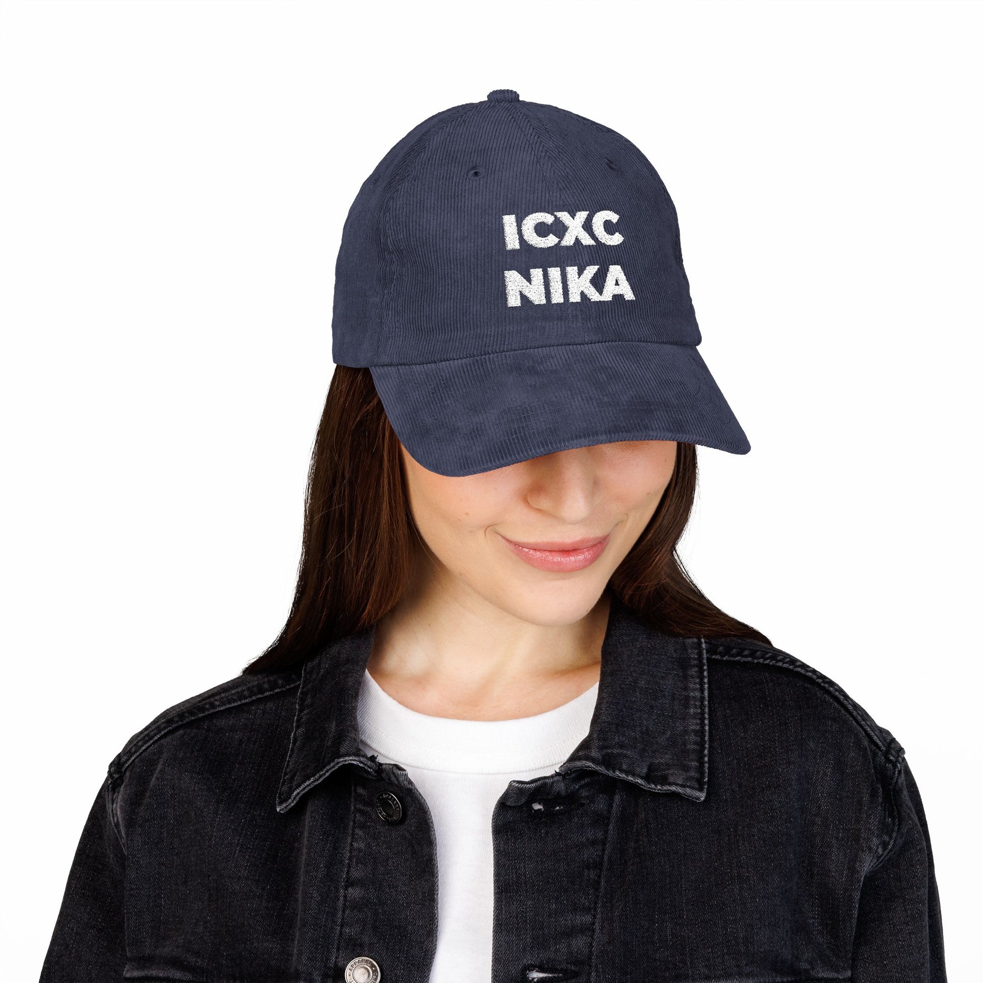 Woman wearing a White ICXC NIKA Text Christogram cap—an embroidered cotton corduroy hat with the Orthodox Christian symbol meaning "Jesus Christ Conquers"—paired with a black denim jacket and white shirt.