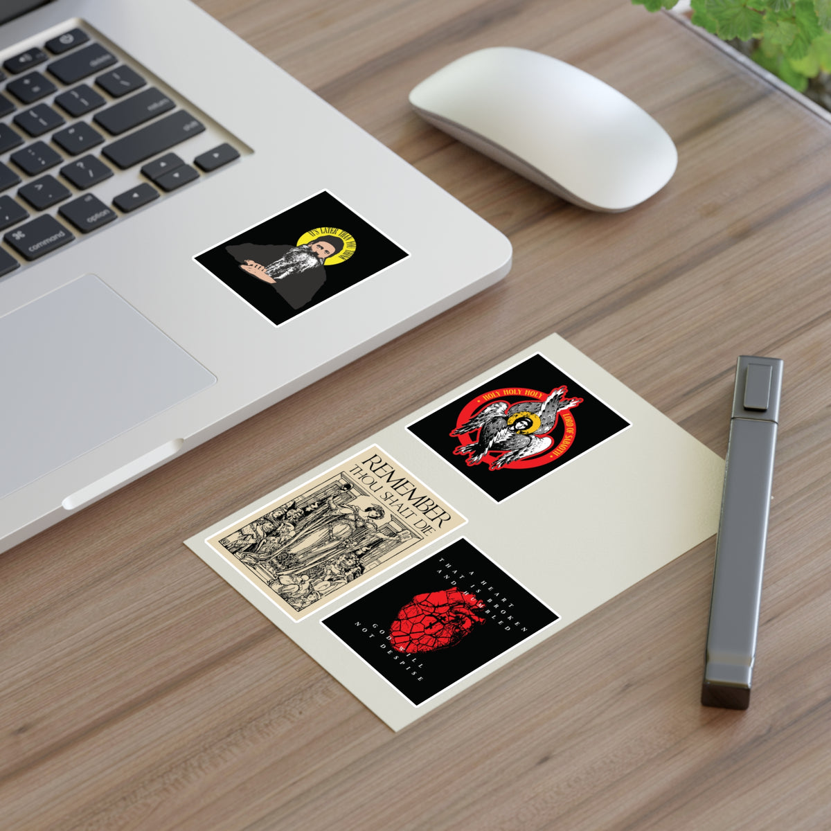 A laptop and pen on a desk with a Bestseller Orthodox Sticker Mix No. 4 postcard featuring four art stickers.