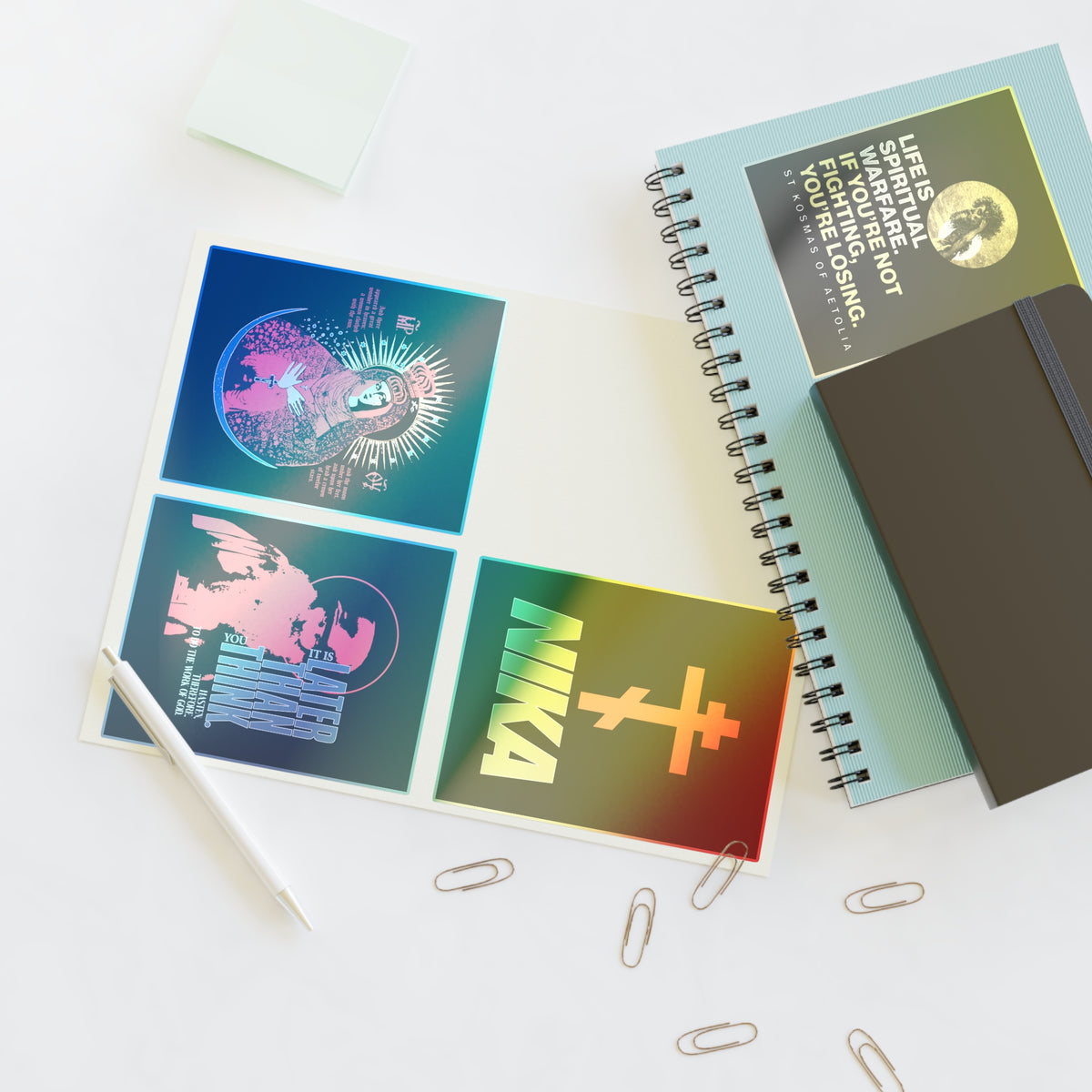 A notebook, sticky notes, Bestseller Orthodox Sticker Mix No. 5, and open folder with graphic cards on a white desk.