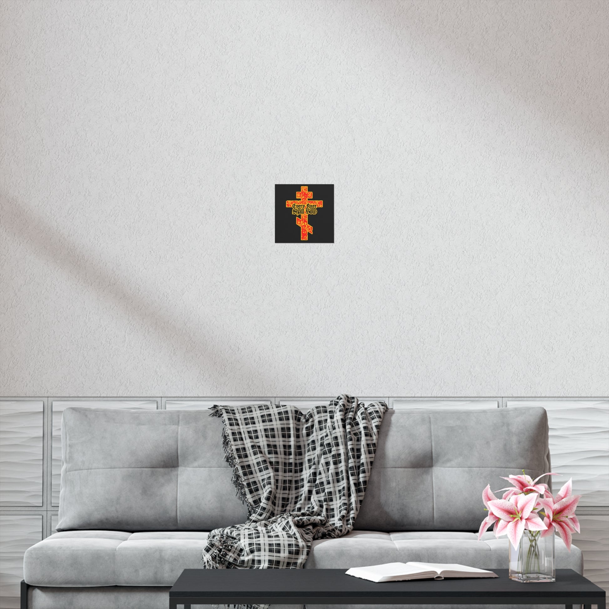 A gray sofa with a plaid blanket, open book, pink flowers, and the "Every Knee Shall Bow" gold and red floral Orthodox cross poster above, creates a peaceful space reflecting righteousness and strength.