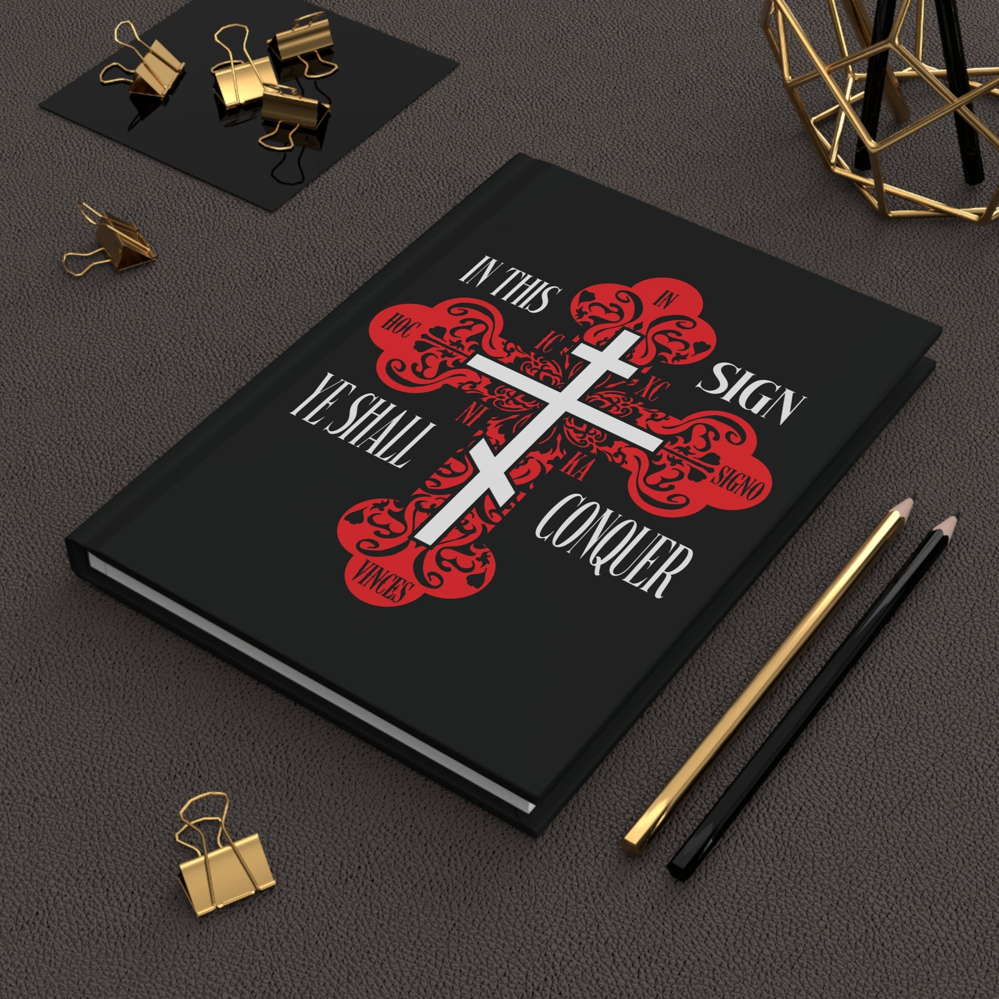 The "In This Sign Ye Shall Conquer" Christian Journal, featuring a red ornate Orthodox cross and the phrase ICXC NIKA, sits on a desk with pencils and clips.