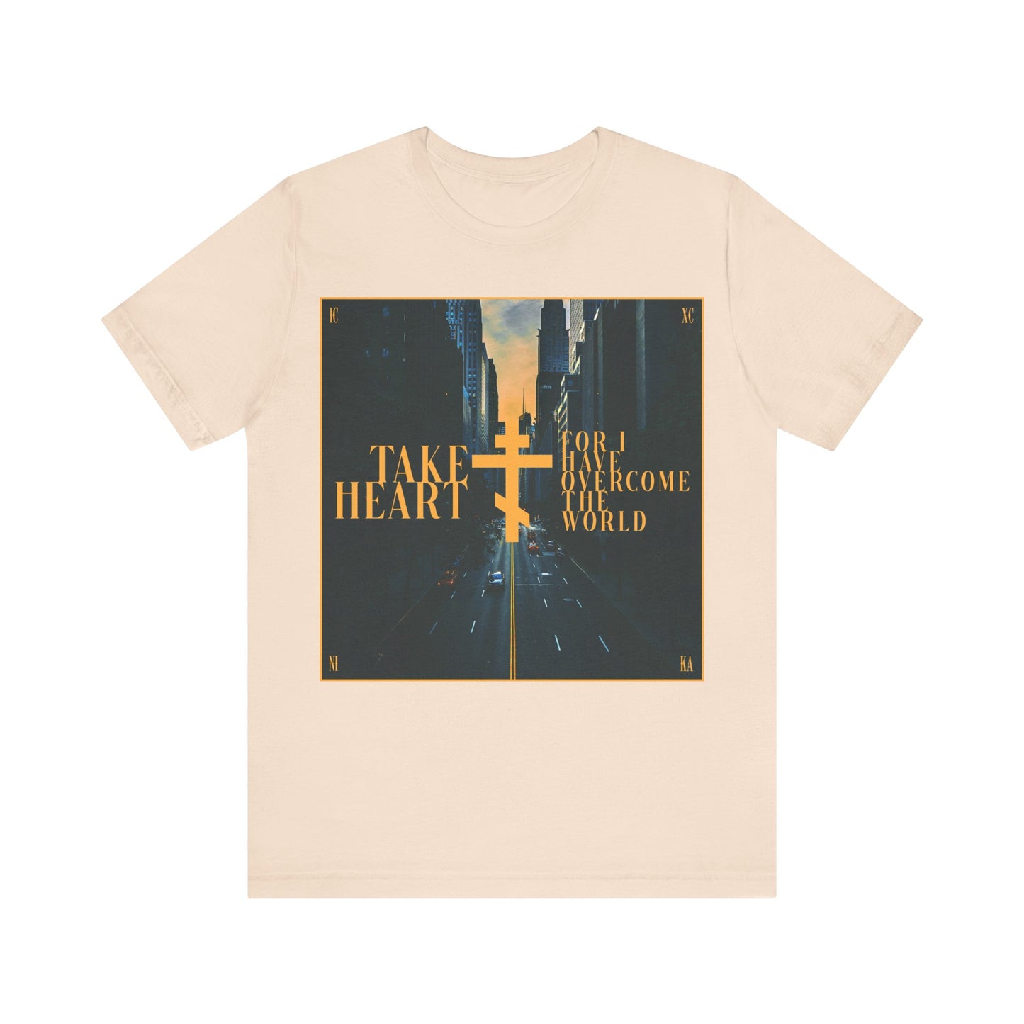 Soft Cream cotton t-shirt featuring a modern city street scene and gold "Take Heart, For I Have Overcome the World" (John 16:33) text—a Redemptive Orthodox Christian design to encourage joy in every challenge.