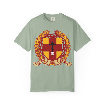 Bay-colored heavyweight cotton unisex t-shirt featuring a heraldic shield design with a red and gold crest, Orthodox cross, skull, and Crown of Thorns, along with a banner reading “First Born from the Dead,” inspired by Colossians 1:18 and the theme of redemption through His blood.