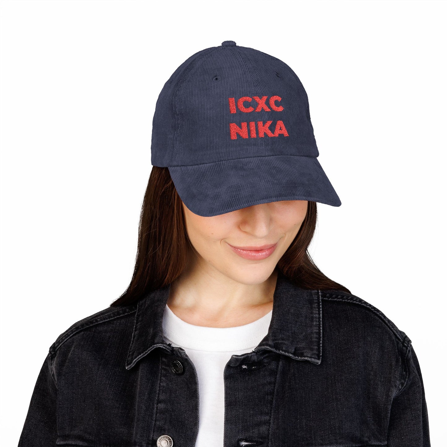 Woman wearing a Red ICXC NIKA Text Christogram embroidered cotton corduroy cap, symbolizing "Jesus Christ Conquers," paired with a white shirt and black denim jacket.