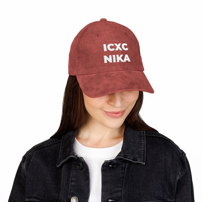 Woman wearing a white ICXC NIKA Christogram cap ("Jesus Christ Conquers")—Orthodox embroidered cotton corduroy—paired with a black denim jacket and white shirt, looking down.