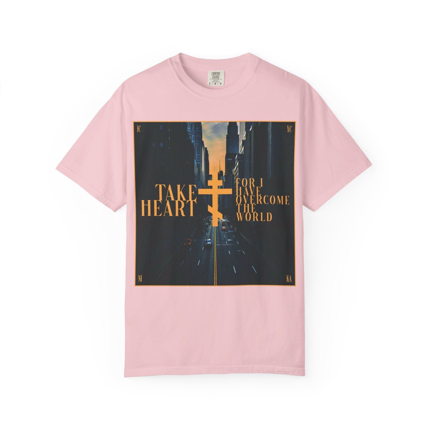 Blossom-colored heavyweight cotton unisex tee featuring a modern city street scene and gold cross, with the message: Take Heart, For I Have Overcome the World (John 16:33)—a reminder that sorrow is turned into joy and encouragement to ask and receive.