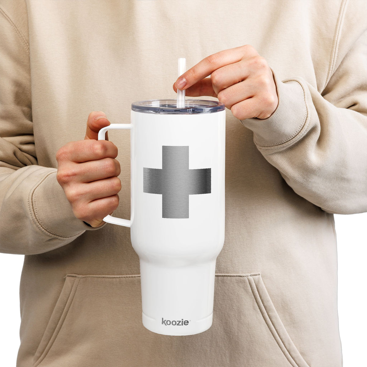 A person wearing a beige hoodie holds the Minimalist Cross Engraved 40oz Koozie Tumbler—an insulated stainless steel travel accessory featuring a white finish, sturdy handle, straw, and subtle gray cross engraving—capturing the essence of Orthodox Christian reverence for the Exaltation of the Cross.