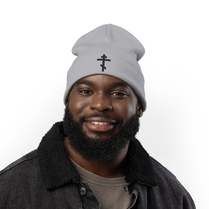 A smiling man with a beard wears a light gray beanie embroidered with the Simple Black Orthodox TriBar Cross and the phrase "Nail My Passions to the Wood of Thy Precious Cross O Lord," paired with a dark jacket.
