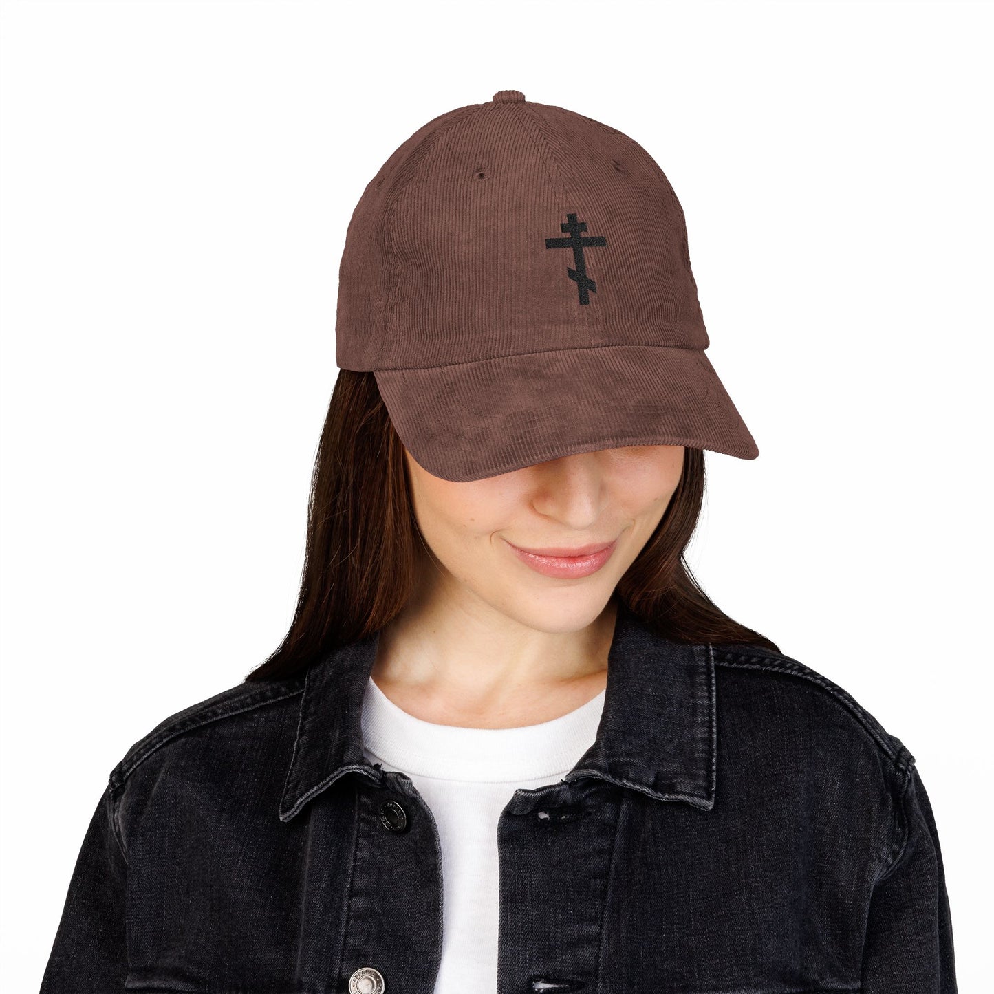 A woman wearing the Simple Black Orthodox TriBar Cross embroidered cotton corduroy cap, paired with a white shirt and black denim jacket, looks down and smiles.