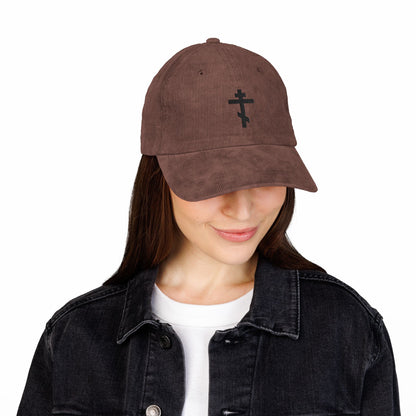 A woman wearing the Simple Black Orthodox TriBar Cross embroidered cotton corduroy cap, paired with a white shirt and black denim jacket, looks down and smiles.