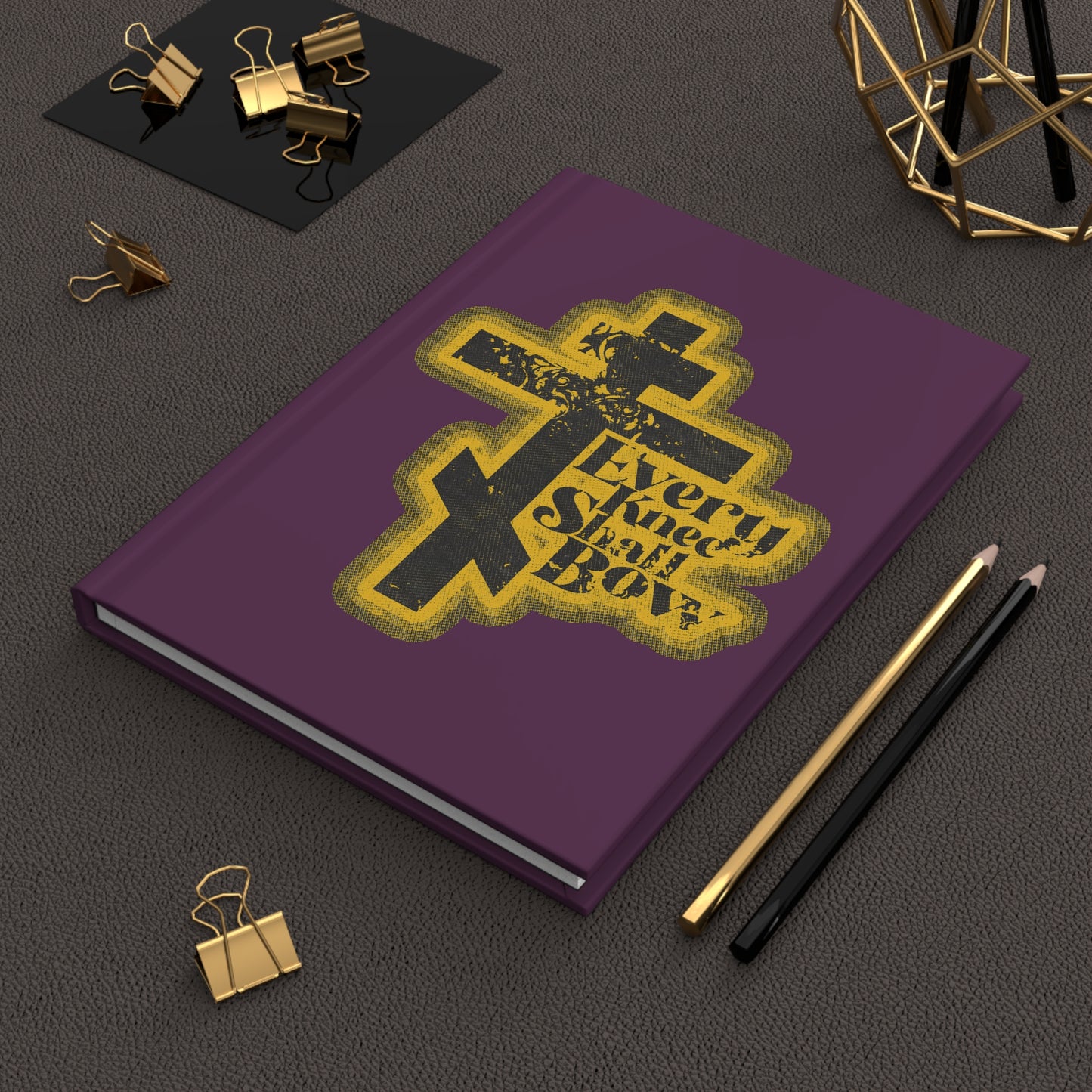 A 70s distressed halftone comic book style journal, "Every Knee Shall Bow" (Philippians 2:10-11, Isaiah 45:23), rests on a desk with pens and gold clips—a unique Orthodox Christian blank notebook.