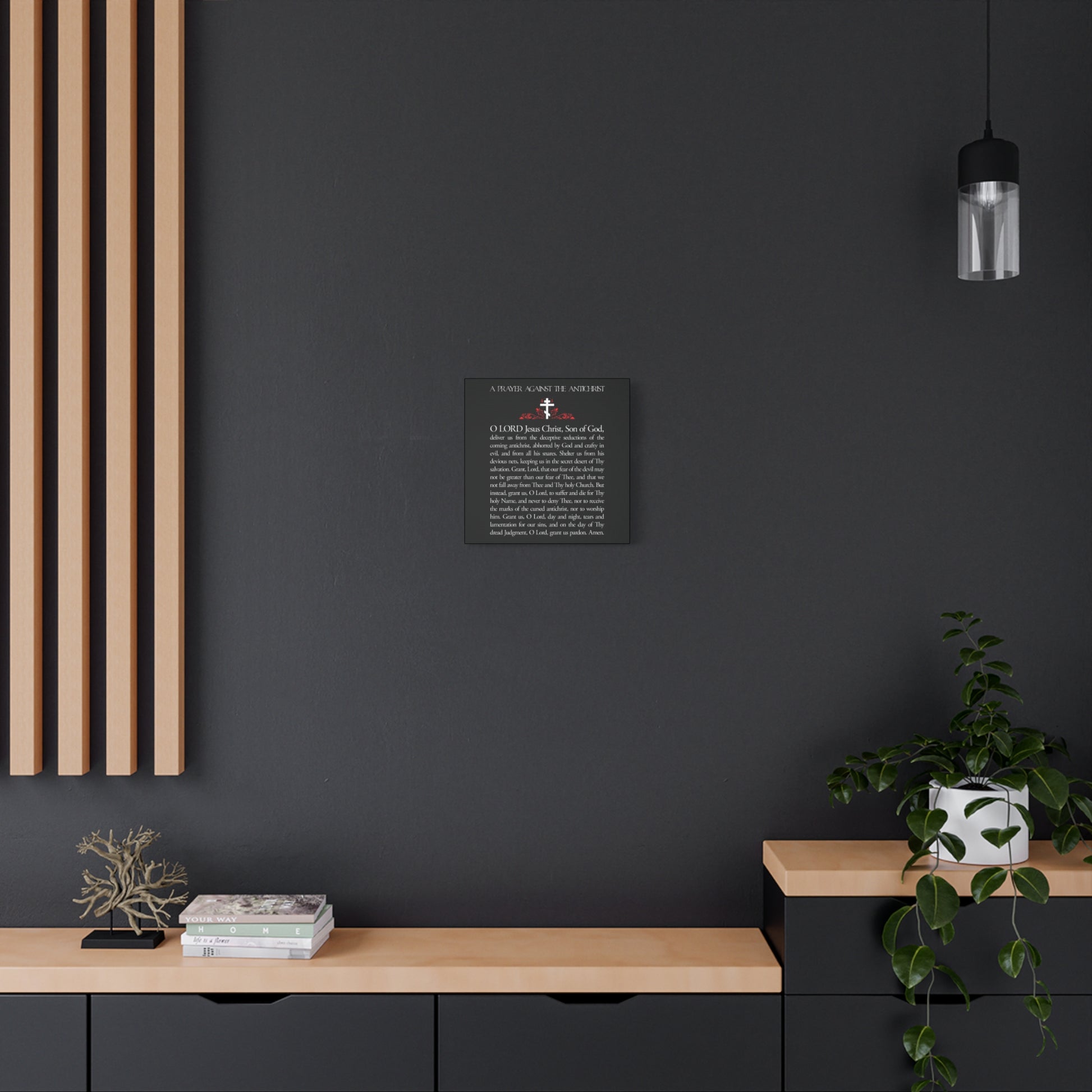 A minimalist interior with black walls, wooden accents, a potted plant, and a framed "Prayer Against the Antichrist By Elder Anatoly the Younger of Optina | Christ is King" Orthodox Christian wall art hangs on the wall.