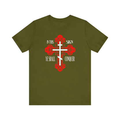 Olive unisex tee featuring an ornate Orthodox cross with red and white details, text "In This Sign Ye Shall Conquer"—inspired by ICXC NIKA and Jesus Christ Conquers. Bold Christian apparel, perfect for those honoring spiritual victory.