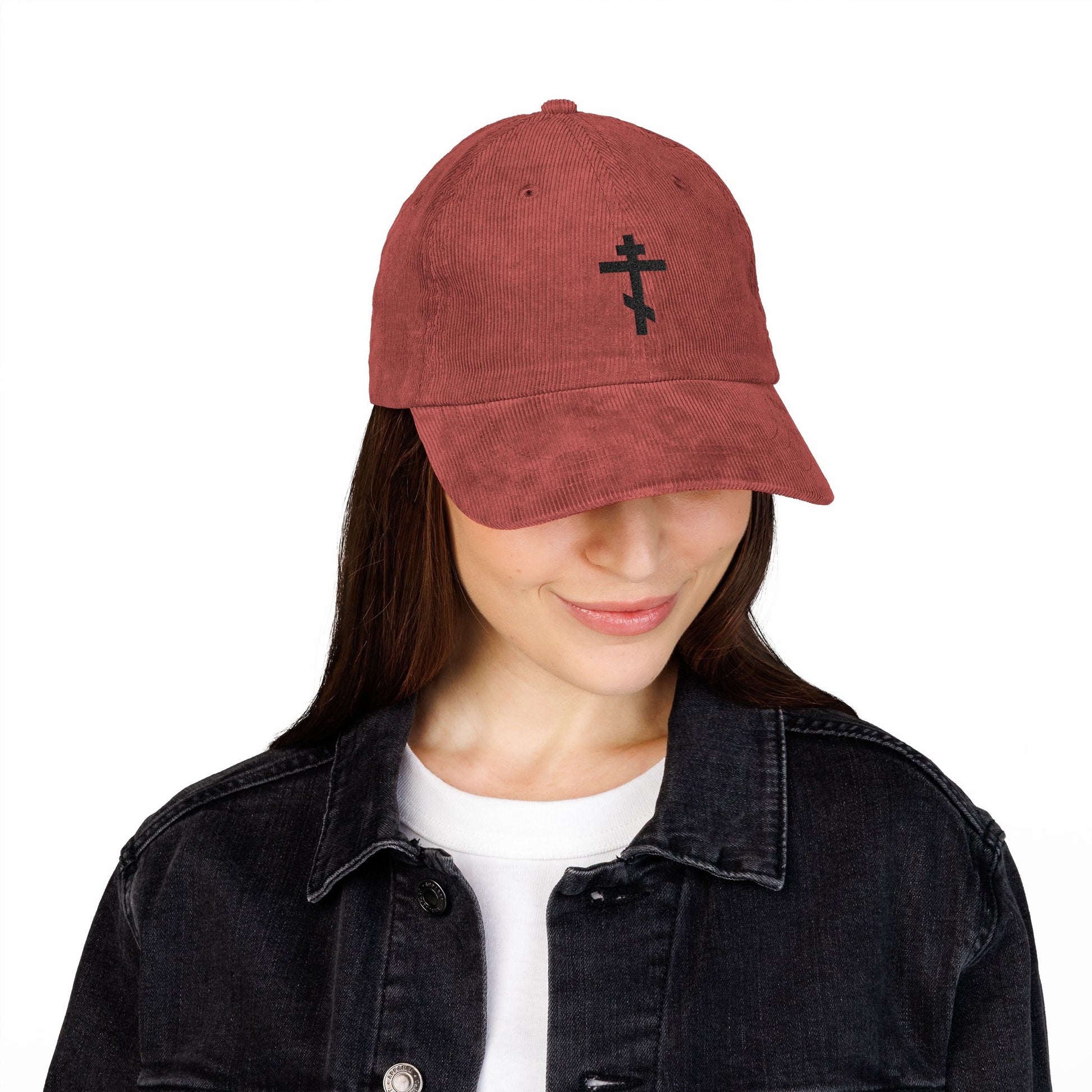 Woman wearing the Simple Black Orthodox TriBar Cross Embroidered Cotton Corduroy Cap, symbolizing unseen warfare that makes demons tremble, paired with a black denim jacket and smiling while looking down.