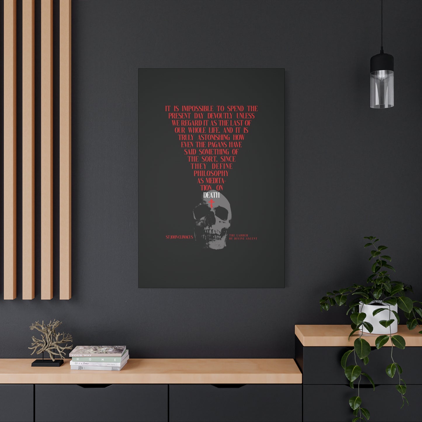 The Present Day As the Last Day of Our Life" canvas wall art, featuring a skull with a red Orthodox cross (inspired by St John Climacus' memento mori), hangs above a desk adorned with books, a plant, and decor on a dark wall.