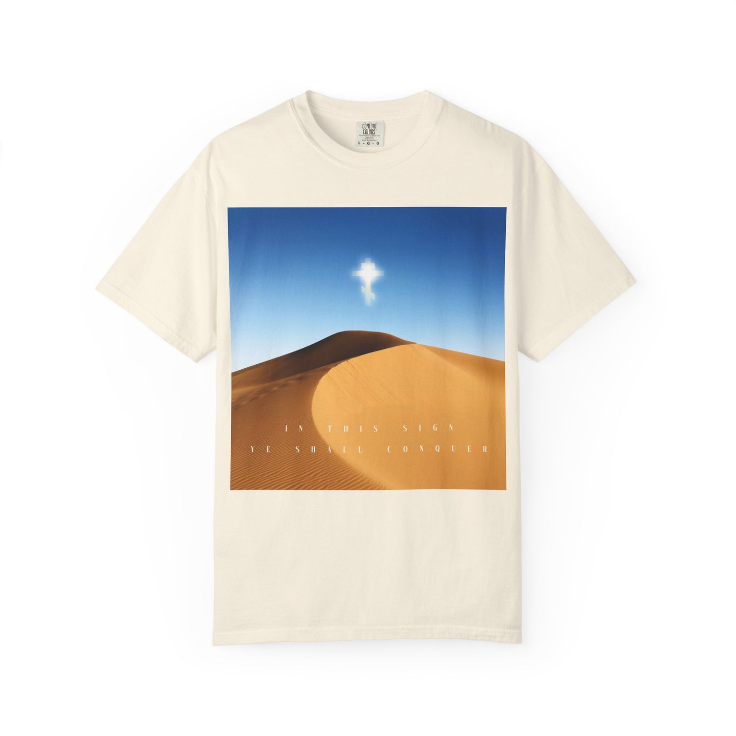 Ivory heavyweight cotton unisex tee, titled "In This Sign Ye Shall Conquer Desert Sun Scene | The Cross is the Might of Kings," featuring a desert sun landscape beneath a radiant cross, inspired by the Elevation of the Cross, and adorned with the words "In This Sign Ye Shall Conquer.