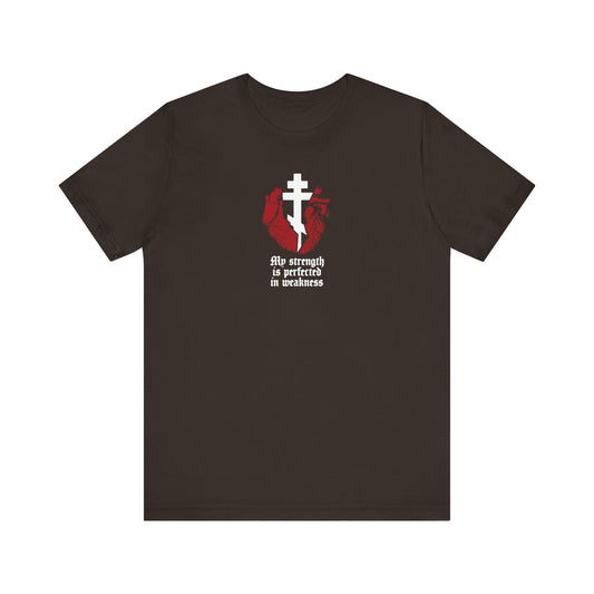 Brown t-shirt featuring a broken heart with a cross and gothic text, "My Strength is Perfected in Weakness" (2 Corinthians 12:9). Orthodox lightweight cotton unisex tee symbolizes strength found through Christ.