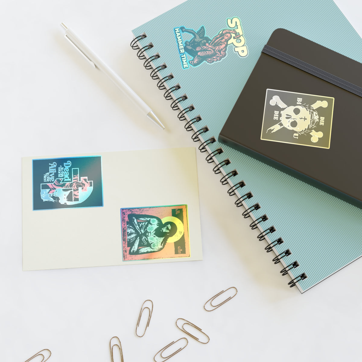 Spiral notebooks, a pen, and Random Mix No. 1 Four Sticker Sheet | Jesus Christ Iconographic displayed on white.