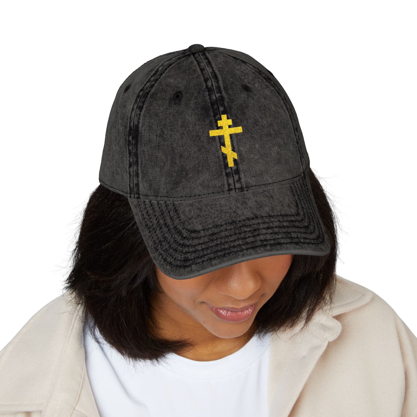 A woman looks downward in quiet reflection, wearing the Simple Yellow Orthodox TriBar Cross minimalist distressed cap with a yellow Orthodox cross embroidered on the front.