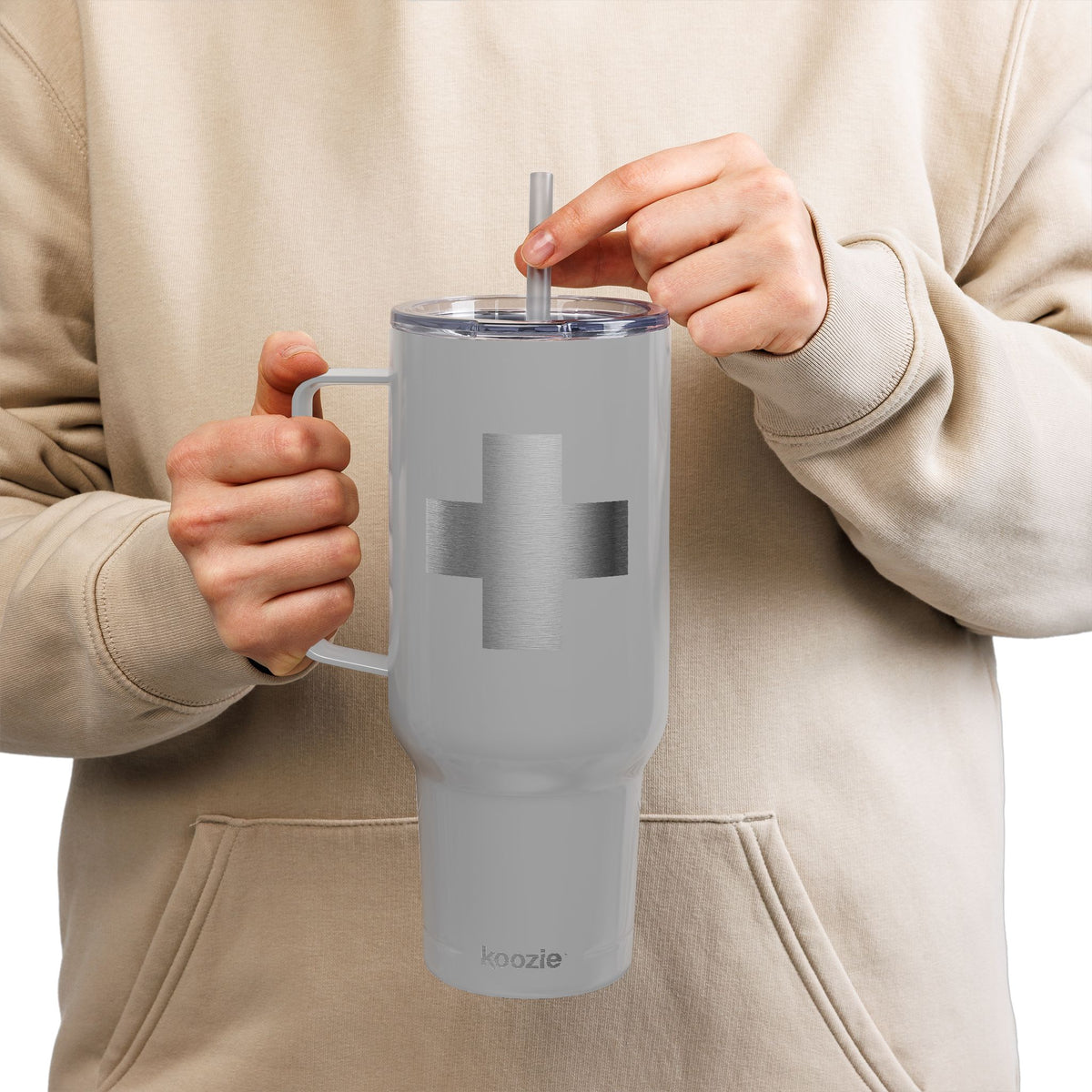 A person in a beige hoodie sips through a straw from a Minimalist Cross Engraved 40oz Koozie Tumbler—an insulated stainless steel Orthodox Christian home and travel accessory, its subtle cross design evoking the spirit of exaltation celebrated during the Exaltation of the Cross.