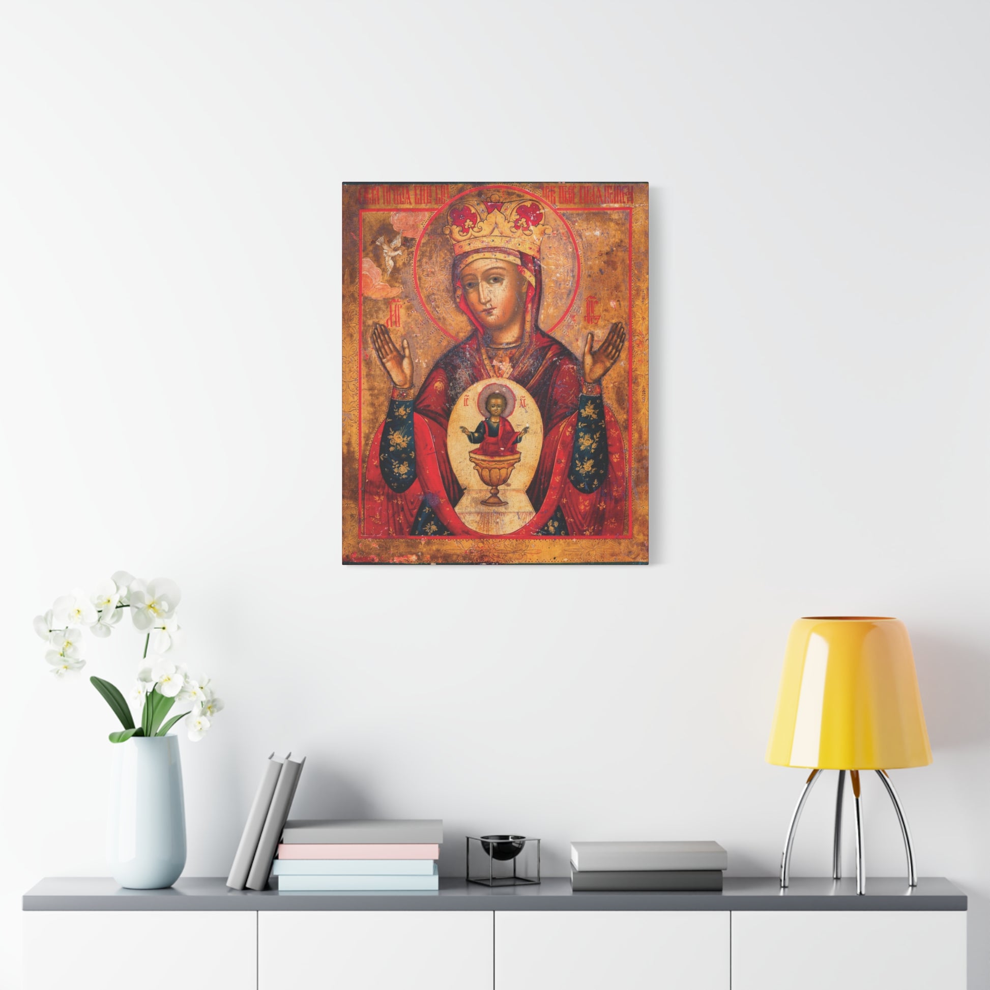 The “Mother of God of Nicaea Russian Orthodox Christian Icon | Panagia | Theotokos Mary | Religious Canvas Sacred Wall Art” is displayed on a white wall above a console table styled as a Holy Table, adorned with books, flowers, and a yellow lamp.