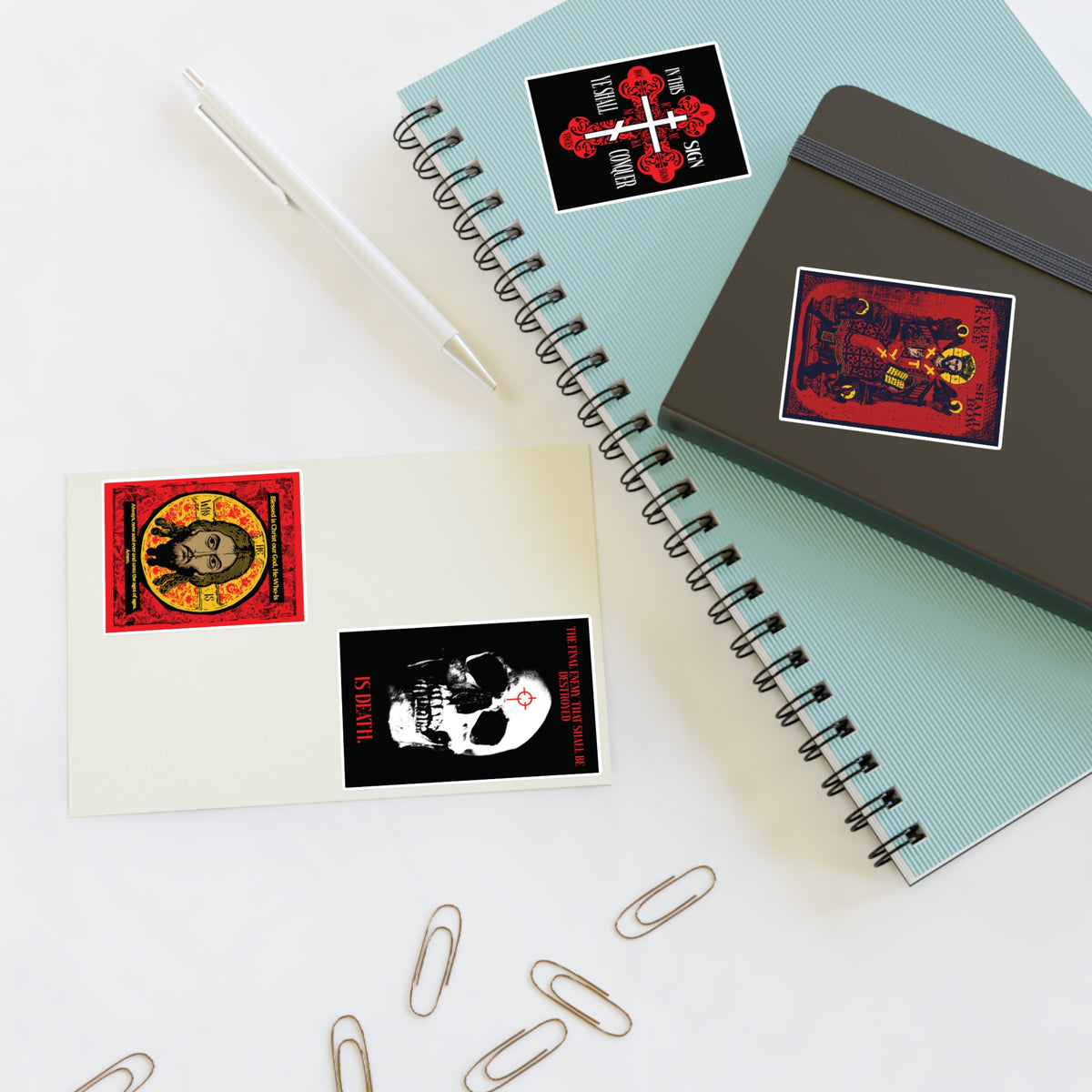 Two spiral notebooks, a pen, paperclips, and Bestseller Orthodox Sticker Mix No. 3 on a white surface.