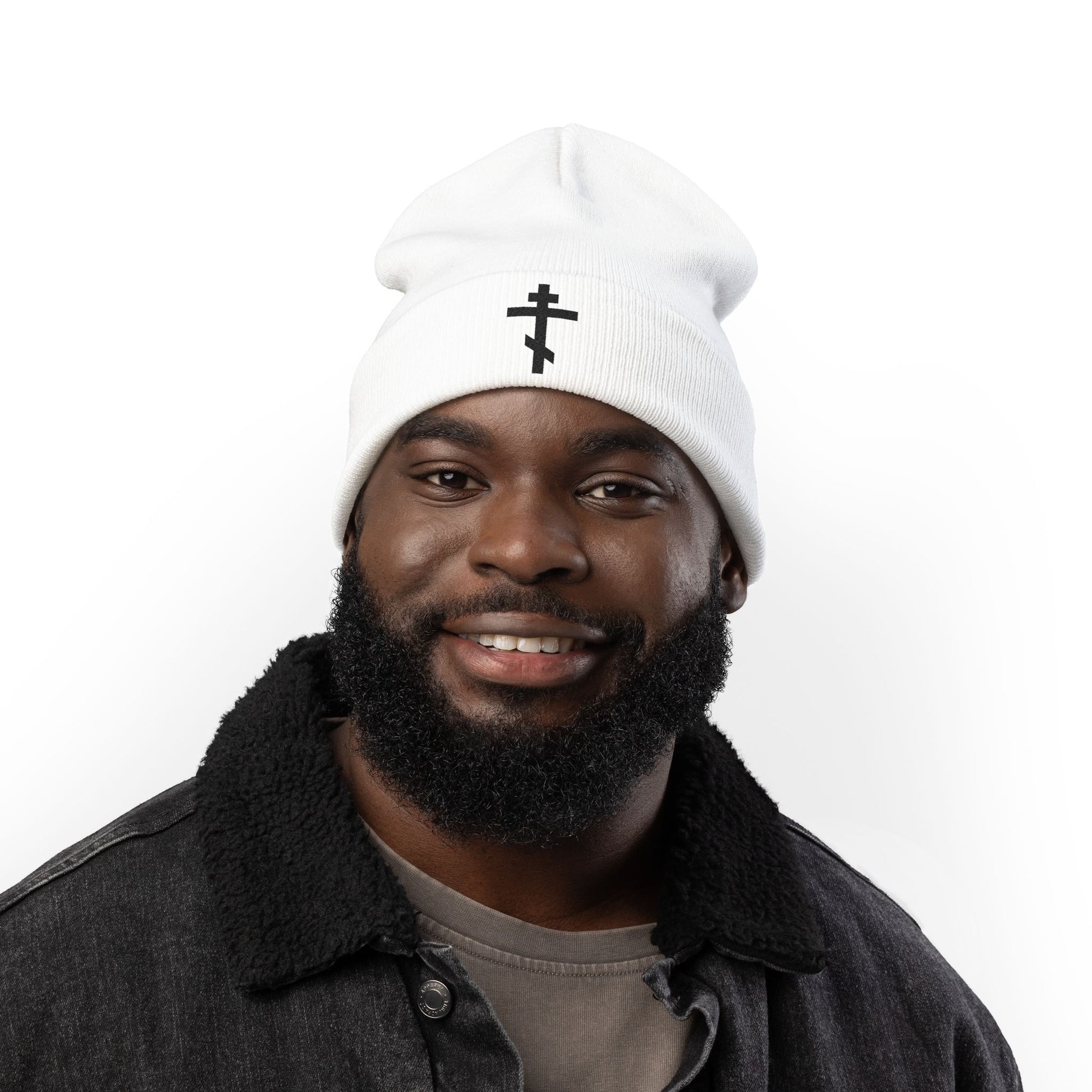 Man smiling in a dark jacket, wearing the "Simple Black Orthodox TriBar Cross | Nail My Passions to the Wood of Thy Precious Cross O Lord" Orthodox Christian embroidered knit beanie against a white background.