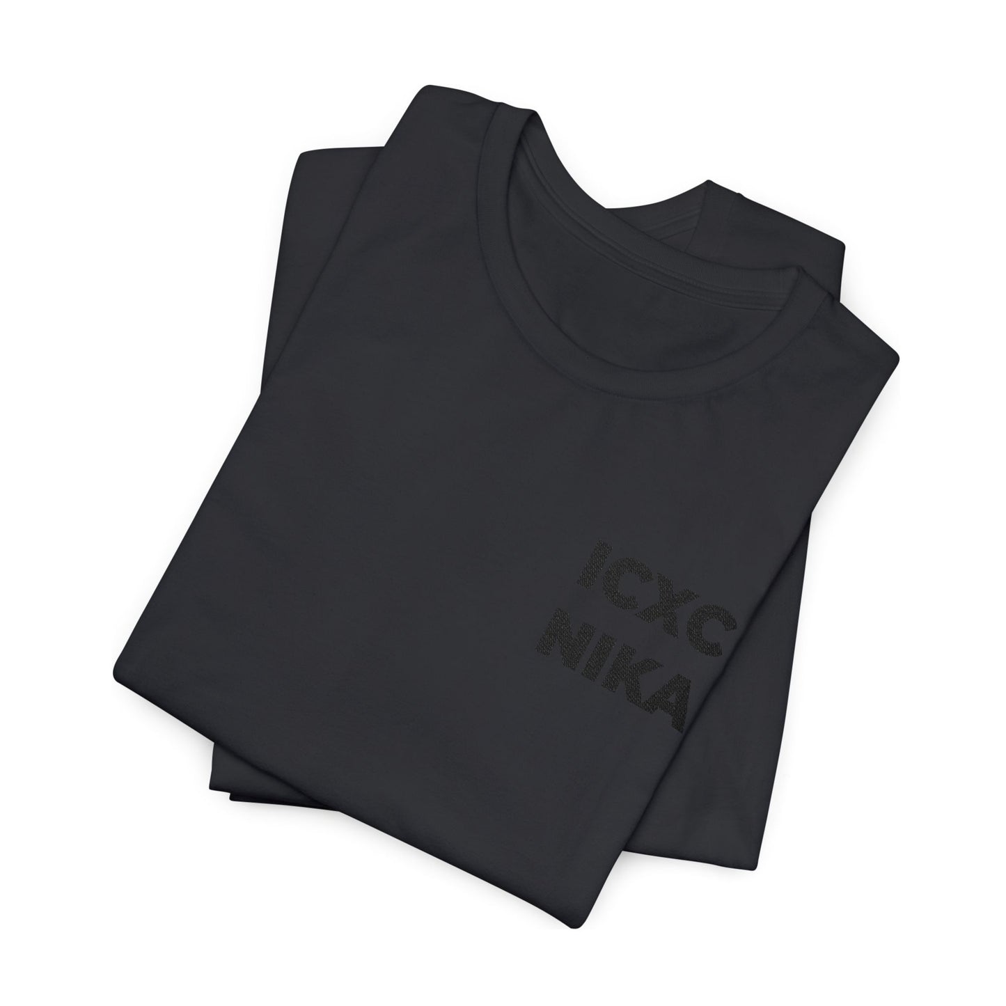 Two black cotton unisex t-shirts, stacked, display the embroidered "ICXC NIKA" Christogram on the chest—an Orthodox symbol meaning "Jesus Christ Conquers.