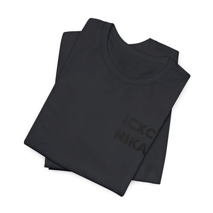 Two black cotton unisex t-shirts, stacked, display the embroidered "ICXC NIKA" Christogram on the chest—an Orthodox symbol meaning "Jesus Christ Conquers.